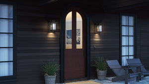 A wooden arched front door with glass panels is flanked by potted plants and Urban Ambiance UQL1643 Craftsman Outdoor Wall Sconces (Peacehaven Collection, 14''H, 8.75''W, Natural Black), with patio chairs nearby.