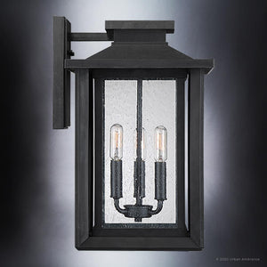 The Urban Ambiance UQL1644 Peacehaven Collection Craftsman Outdoor Wall Sconce features a 17''H x 10.75''W marine-grade black metal frame with clear glass panels and three exposed bulbs, mounted on a flat rectangular base.
