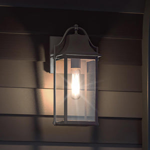 The Urban Ambiance UQL1671 Vintage Outdoor Wall Sconce (14.75''H x 7''W) from the Eastbourne Collection features an Estate Bronze finish and marine-grade construction, mounted on a paneled wall to illuminate the outdoor area.