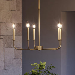 A gorgeous UQL3802 Modern Farmhouse Chandelier with an Olde Brass Finish from the Bideford Collection by Urban Ambiance hanging in a room with a potted plant.
