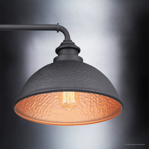 A close-up of the Urban Ambiance UHP1177 Hammered Outdoor Wall Light from the Firenze Collection showcases its dome-shaped silhouette and visible Edison bulb, casting a warm glow against a gradient background. The midnight black finish enhances its striking industrial design, making this 10-3/8″ x 12″ fixture both stylish and functional.