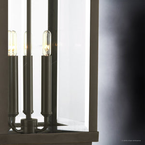Close-up of the UHP1190 Colonial Outdoor Post / Pier Light from Urban Ambiance’s Calderdale Collection, featuring a modern black metal and glass design with exposed bulbs in an Olde Bronze finish; positioned against a reflective glass and dark gradient background, it echoes the form of a classic beveled glass lantern reimagined with contemporary style.