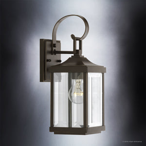 Introducing the UHP1192 Colonial Outdoor Wall Light from the Calderdale Collection by Urban Ambiance, this 15-1/8″ x 5-1/2″ lantern features a Colonial-inspired design with an Olde Bronze finish. The wall-mounted fixture showcases a metal frame paired with clear beveled glass panels and a visible bulb, all set against a gray gradient background.