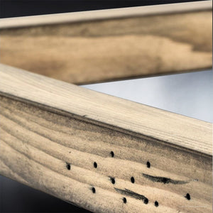 Close-up of two intersecting wooden beams with visible wood grain and small black holes on one piece, set against a blurred background, capturing the rustic charm reflected in the Brighton Collection’s UHP2743 Modern Farmhouse Pendant Light (12-1/4″ x 10″, Galvanized Steel Finish) by Urban Ambiance.