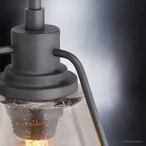 Close-up of the Urban Ambiance UHP2993 Industrial Pendant Light from the Rochdale Collection, showcasing an industrial-chic design with a charcoal finish metal frame, clear seeded glass shade, and a visible glowing bulb inside (13″ x 13″).