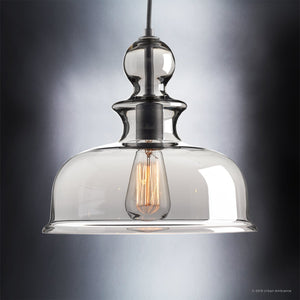 The Urban Ambiance UHP3041 Modern Farmhouse Pendant Light from the Dundee Collection, featuring an 11-1/4″ x 12″ clear glass shade and a charcoal finish, hangs gracefully from a cable against a softly lit gradient background, highlighting the refined beauty of handcrafted artistry.