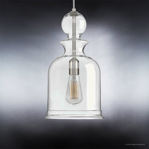 The UHP3043 Modern Farmhouse Pendant Light from the Dundee Collection by Urban Ambiance features a clear, hand-blown glass shade that showcases a visible filament bulb, suspended gracefully against a dark gradient background. Its brushed nickel finish brings a modern touch of elegance.